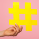Hand holding a yellow hashtag in front of a pink background