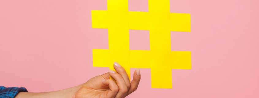 Hand holding a yellow hashtag in front of a pink background