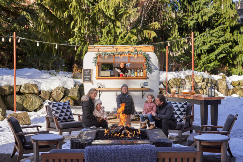 Vintage camper outdoors in the snow with people sitting around a fire