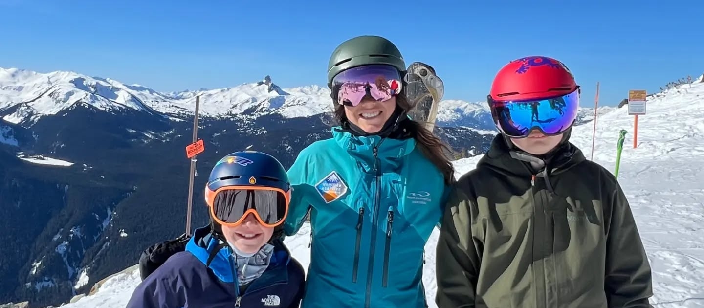 A Whistler Adaptive Ski Instructor smiling with her ski students at the top of Whistler Mountain